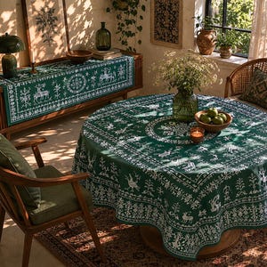 May include: A dark green tablecloth and matching table runner featuring a white folk-art style print of deer, birds, and geometric floral patterns. The fabric has a repeating border design and a central circular motif, creating a cohesive look.