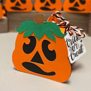 May include: Orange and green paper pumpkin treat box with a black and white twine bow and a tag that says "trick or treat".