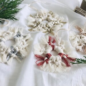 Peut inclure: Quatre ornements en macram&eacute; faits &agrave; la main en forme de flocons de neige avec des accents de diff&eacute;rentes couleurs. Les ornements sont blancs avec des accents argent&eacute;s, dor&eacute;s et rouges. Les ornements sont suspendus &agrave; un fond blanc.