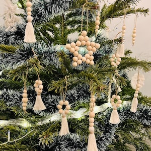 Könnte beinhalten: Ein geschmückter Weihnachtsbaum mit verschiedenen Holzornamenten. Die Ornamente umfassen Perlenstränge, Sternformen und Quasten, alle in natürlichen Holztönen. Der Baum ist grün mit Lametta und Lichtern.