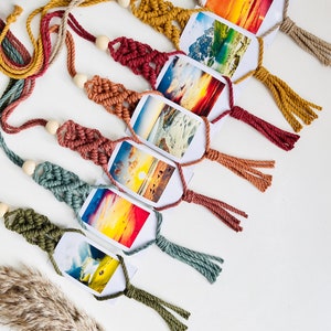 May include: A string of macrame photo holders with colorful tassels and wooden beads. Each holder features a different landscape photograph.
