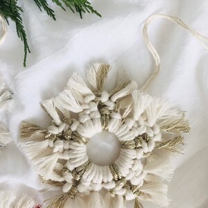 Peut inclure: Une d&eacute;coration de flocon de neige en macram&eacute; blanc et or avec un centre circulaire. Le flocon de neige est fait avec un cordon blanc &eacute;pais et a des accents dor&eacute;s.