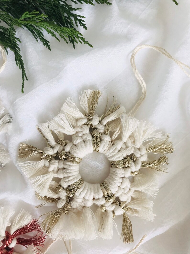 Peut inclure: Une d&eacute;coration de flocon de neige en macram&eacute; blanc et or avec un centre circulaire. Le flocon de neige est fait avec un cordon blanc &eacute;pais et a des accents dor&eacute;s.