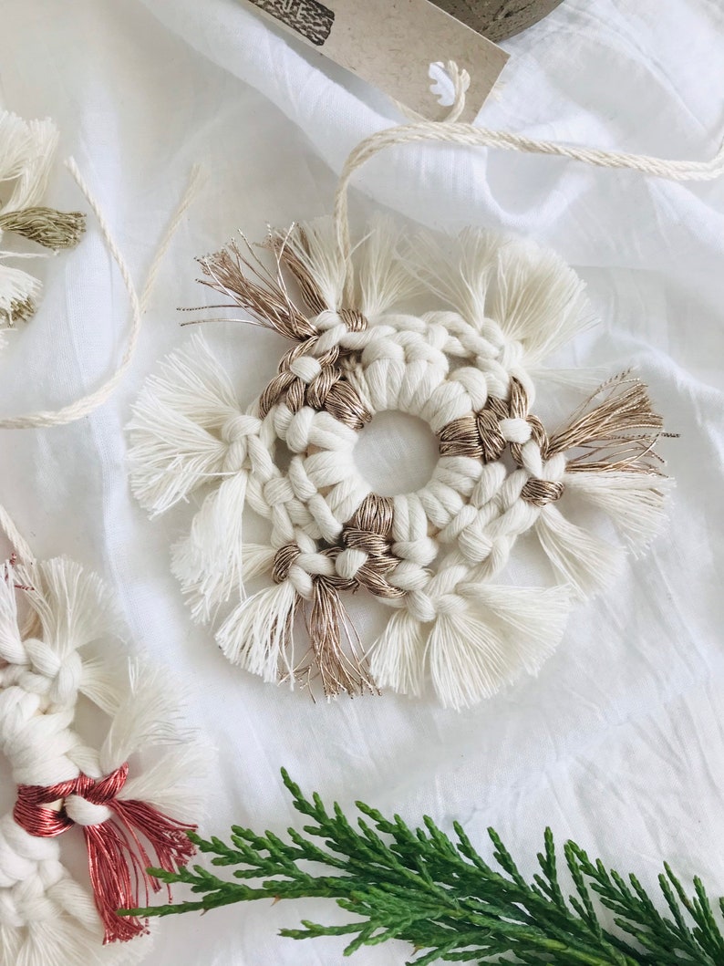 Peut inclure: Une d&eacute;coration en macram&eacute; blanche et dor&eacute;e de forme circulaire avec des d&eacute;tails en franges. L'ornement est fait &agrave; la main et a un style rustique et boh&egrave;me.
