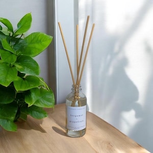 May include: A clear glass bottle diffuser with wooden sticks, filled with a light yellow liquid. The bottle has a white label with the text "bergamot & grapefruit" printed on it.