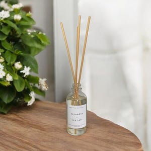 May include: A clear glass bottle diffuser with wooden sticks, filled with a lavender and sea salt scented oil. The bottle has a white label with the text "lavender & sea salt" printed on it.