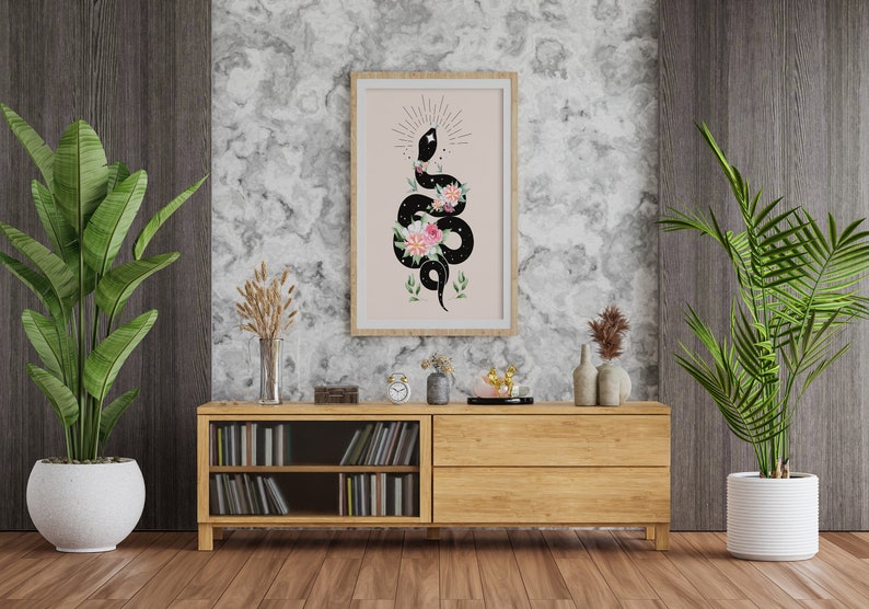 May include: A framed print of a black snake with pink and white flowers on a pink background. The snake is coiled and has a star on its head. The print is hanging on a wall with a wooden shelf below it.
