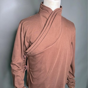 Puede incluir: Una camisa marrón de manga larga con cuello alto y un diseño drapeado único. Las mangas están fruncidas en las muñecas.