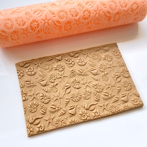 May include: A close-up of a silicone rolling pin with a seashell and starfish design. The rolling pin is used to create an embossed pattern on a piece of brown fondant.
