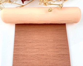 May include: A close-up of a light pink faux leather sheet rolled up. The sheet has a wood grain texture.