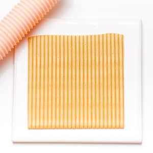 May include: A white rectangular baking mat with a raised, textured surface. The surface has a series of parallel ridges that create a grooved pattern. The mat is designed for use in baking and creating decorative patterns on food.
