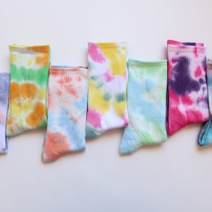 May include: Eight pairs of colorful tie-dye socks in various shades of blue, green, pink, orange, and yellow. The socks are folded and arranged in a row on a white background.