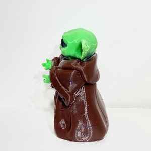 Peut inclure: Une figurine imprim&eacute;e en 3D d'un personnage de la franchise Star Wars, de couleur verte et marron. Le personnage porte une robe marron et a de grandes oreilles.