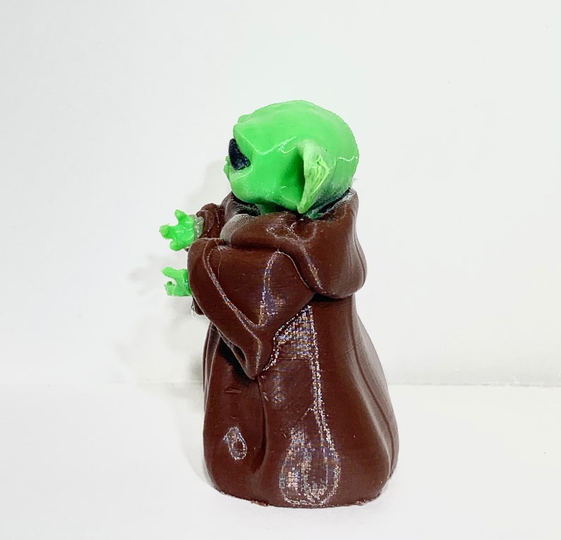 Peut inclure: Une figurine imprim&eacute;e en 3D d'un personnage de la franchise Star Wars, de couleur verte et marron. Le personnage porte une robe marron et a de grandes oreilles.