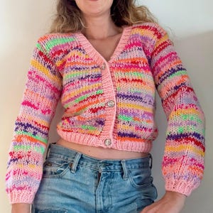 Könnte beinhalten: Ein rosa, mehrfarbig gestreifter Cardigan mit Knopfleiste. Der Cardigan hat einen V-Ausschnitt und lange Ärmel.