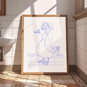 May include: A framed wall art print featuring a blue line drawing of a goose wearing a towel wrapped around its head like a turban. The goose is standing on a grid pattern surface, rendered in a simple, clean illustration style on a white background.