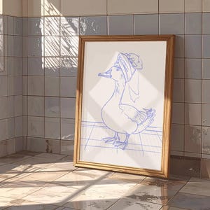 May include: A framed art print featuring a blue line drawing of a goose wearing a towel wrapped around its head like a turban. The goose stands on a grid pattern floor. The frame is made of light-coloured wood with a simple, clean profile.