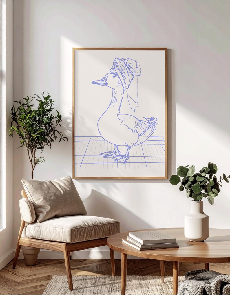 May include: A framed wall art print featuring a blue line drawing of a duck wearing a towel wrapped around its head. The duck stands on a blue grid pattern against a white background, enclosed in a thin, light-coloured wooden frame.