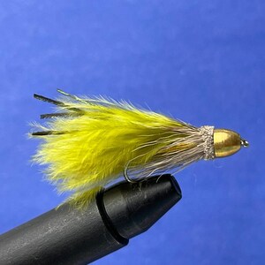 May include: A fishing fly with a yellow feather body, a gold-coloured head, and a silver hook. The fly also has black and brown accents. The fly is designed for catching fish.