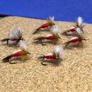 May include: Six red and white fly fishing lures with white and brown feathers.