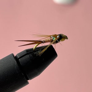 Könnte beinhalten: Nahaufnahme einer Fliegenfisch-Köder mit einem Kupferdrahtkörper, braunen Federn und einem grün schimmernden Kopf.