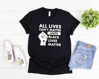 May include: Black t-shirt with a white graphic that reads "All Lives Can't Matter Until Black Lives Matter". The graphic also includes a raised fist with a heart in the center.