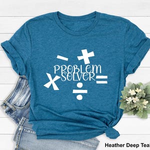 May include: A teal blue t-shirt with white text that reads "Problem Solver" and is surrounded by math symbols: plus, minus, multiply, and divide.