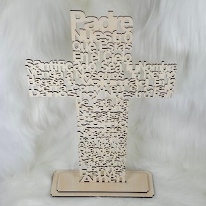Puede incluir: Una cruz de madera clara con las palabras "Padre Nuestro" y otro texto recortado. La cruz se apoya sobre una base rectangular. El texto est&aacute; en espa&ntilde;ol.