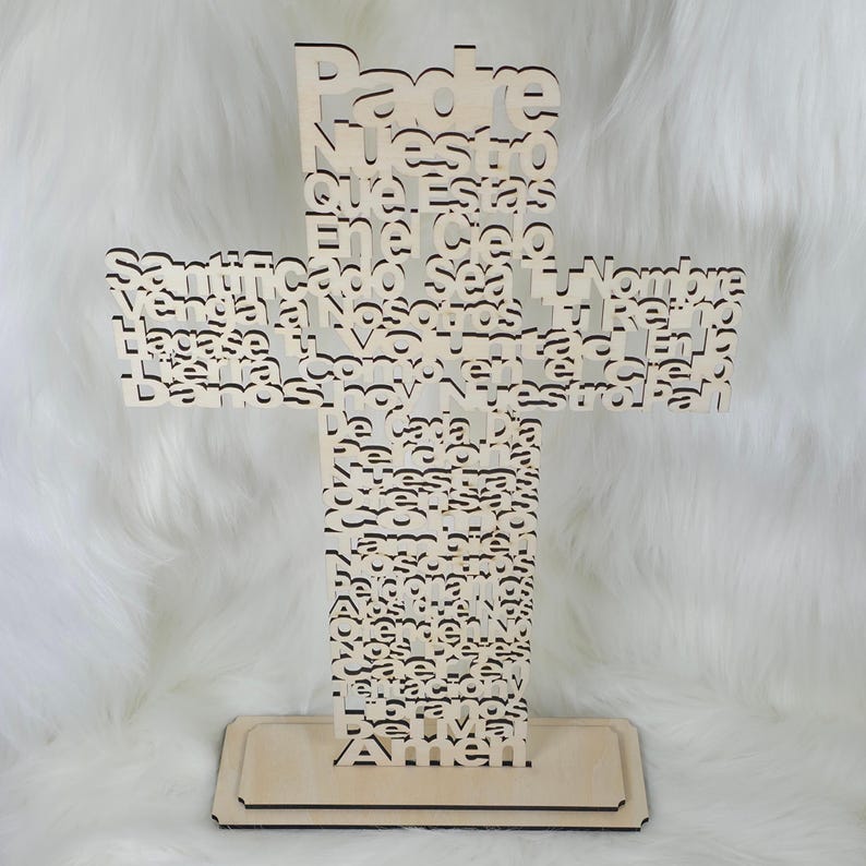 Puede incluir: Una cruz de madera clara con las palabras "Padre Nuestro" y otro texto recortado. La cruz se apoya sobre una base rectangular. El texto est&aacute; en espa&ntilde;ol.