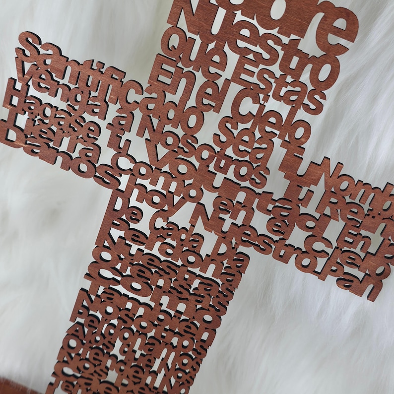 Puede incluir: Una cruz de madera con acabado marr&oacute;n oscuro. La cruz est&aacute; hecha de letras individuales que forman una oraci&oacute;n. La cruz se muestra sobre un fondo blanco y esponjoso.