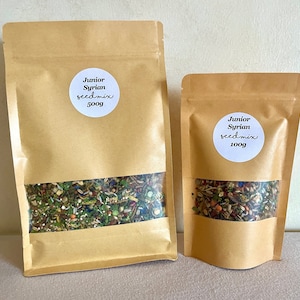 Puede incluir: Dos bolsas de papel marr&oacute;n llenas de una mezcla de semillas. La bolsa m&aacute;s grande est&aacute; etiquetada "Junior Syrian seed mix 500g" y la bolsa m&aacute;s peque&ntilde;a est&aacute; etiquetada "Junior Syrian seed mix 100g".