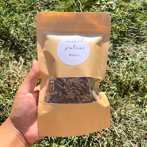 May include: A brown paper bag with a white circle label that says "animal protein mix". The bag contains a variety of dried insects.