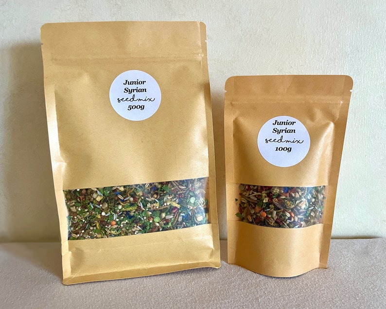 Pu&ograve; includere: Due sacchetti di carta marrone pieni di un mix di semi. Il sacchetto pi&ugrave; grande &egrave; etichettato "Junior Syrian seed mix 500g" e il sacchetto pi&ugrave; piccolo &egrave; etichettato "Junior Syrian seed mix 100g".