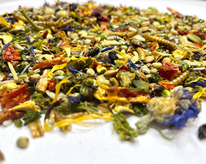 Puede incluir: Primer plano de una mezcla de hierbas, semillas y flores secas. La mezcla incluye hojuelas de pimiento rojo, p&eacute;talos de flores amarillas y hierbas verdes.