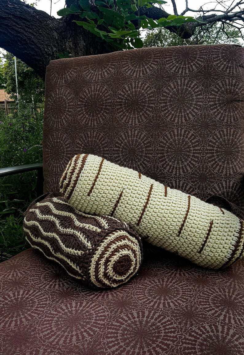 May include: Two crocheted log-shaped pillows, one brown and white with a wavy pattern and the other beige and brown with a striped pattern, are sitting on a brown patterned chair.