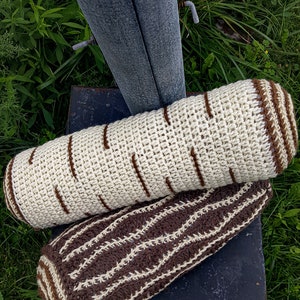 May include: Two crocheted log pillows, one with a brown and white striped pattern and the other with a white base and brown stripes to resemble birch bark.