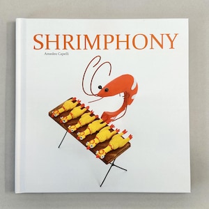 以下が含まれることがあります： 「Shrimphony」というタイトルの本。表紙には、漫画の海老と、焼き台に乗った黄色いラバーチキンが描かれています。オレンジ色の文字でタイトルが書かれた、白を基調としたデザインです。