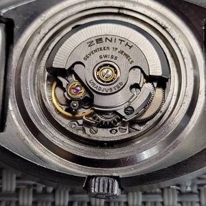 May include: Close-up of a silver Zenith watch movement with the text "Seventeen 17 Jewels Swiss Unadjusted" visible.