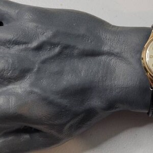 May include: A gold-tone wristwatch with a white face and black leather band. The watch has a moon phase complication and a date window.