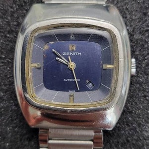 May include: A silver Zenith automatic wristwatch with a blue face and a silver metal band.