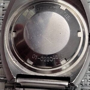 May include: Close-up of the back of a silver wristwatch with a stainless steel band. The watch face has the text "Stainless Steel" and the number "01-0260-463".
