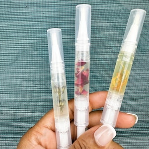 May include: Three clear plastic tubes with white caps containing a clear liquid and dried flowers. The tubes are held in a hand.