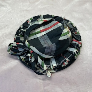 Puede incluir: Un sombrero de cuadros negros y blancos con ribete verde y rojo. El sombrero tiene un borde con volantes y un lazo en un lado.