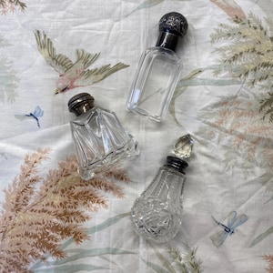May include: Three vintage glass perfume bottles with silver stoppers. The bottles are clear and have a variety of shapes and designs.