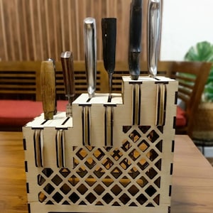 Könnte beinhalten: Ein Holz-Messerblock mit einem Gittermuster auf der Unterseite und Schlitzen zum Halten von Messern. Der Block ist aus hellem braunem Holz gefertigt und hat eine natürliche Oberfläche. Es befinden sich sechs Messer im Block, darunter ein Kochmesser, ein Gemüsemesser und ein Brotmesser.