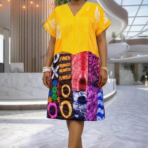 Peut inclure: Robe jaune à col en V avec des manches courtes et une jupe patchwork. La jupe présente divers motifs de tissus colorés. La personne porte des baskets blanches et des boucles d'oreilles blanches. L'arrière-plan est un intérieur de bâtiment moderne.