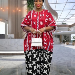 Op de afbeelding: Een rood, wit en zwart patroonjurk met een bijpassende hoofddoek. De jurk heeft een witte handtas. De jurk heeft een uniek ontwerp met een mix van geometrische en abstracte patronen. De outfit is geschikt voor speciale gelegenheden.