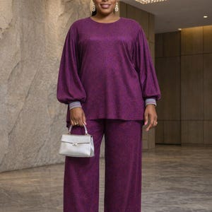May include: A sparkling purple two-piece ensemble, comprising a top with voluminous sleeves and wide-leg trousers. The outfit is complemented by a silver handbag and embellished sandals. The outfit is suitable for formal events.