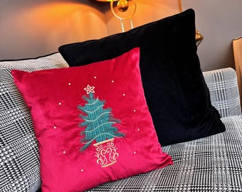 Può includere: Un cuscino in velluto rosso con un ricamo a forma di albero di Natale verde. Il cuscino è su un divano a quadri bianco e nero.