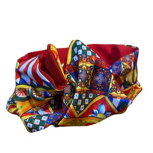Peut inclure: Un bandeau rouge avec un motif coloré composé de formes géométriques et de motifs floraux. Le motif rappelle les carreaux de majolique italiens.